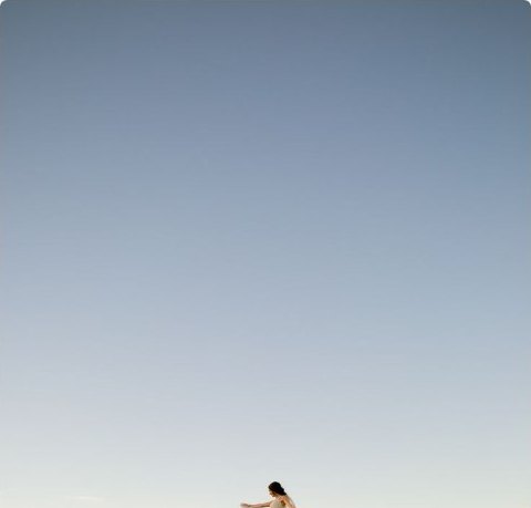 A figure walking through tall grass under a pale open sky