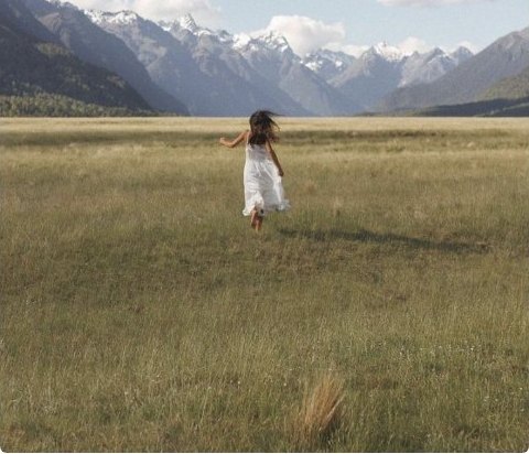 A figure running through a wide valley toward snow-capped mountains