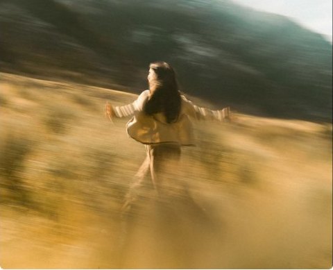 A figure running through a golden hillside, arms open, motion-blurred