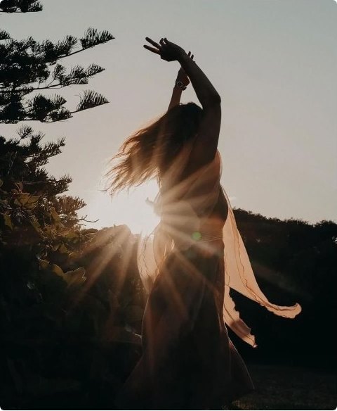 A figure dancing into the sun on a headland at golden hour