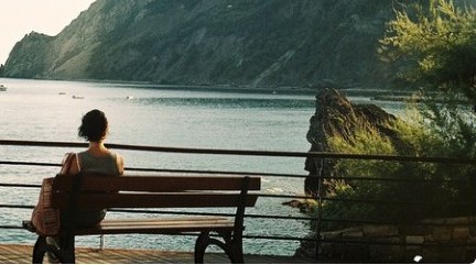 A person on a bench looking out over a green coastal cliff and sea