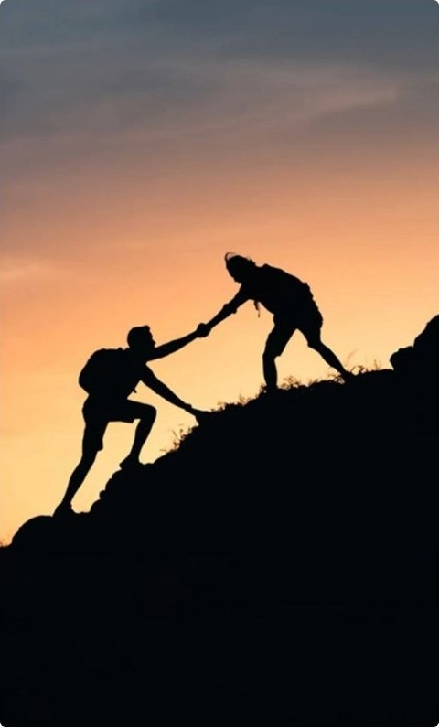 One climber reaching down to help another up a ridge at sunset