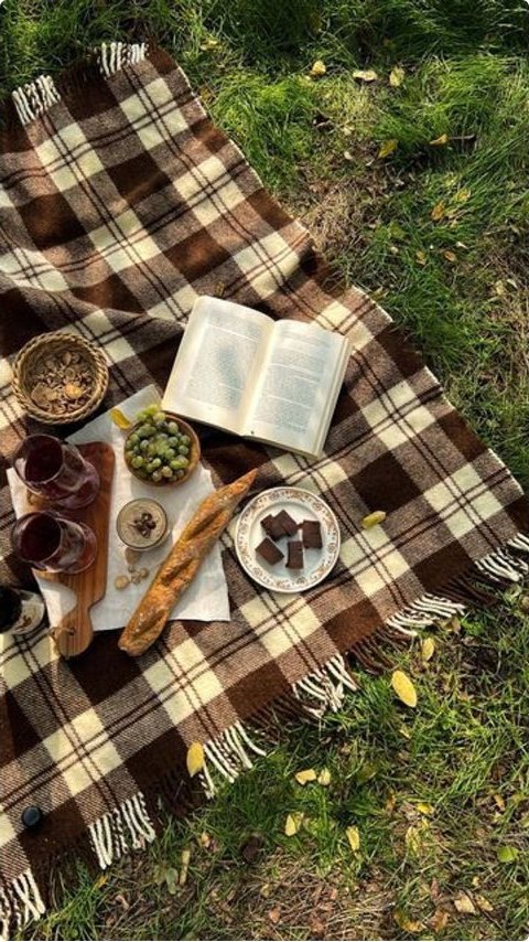 A picnic blanket spread on autumn grass with bread, fruit and an open book