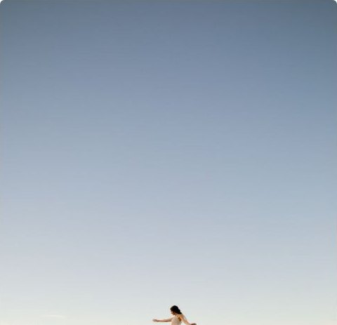 A figure walking through tall golden grass under a wide pale sky