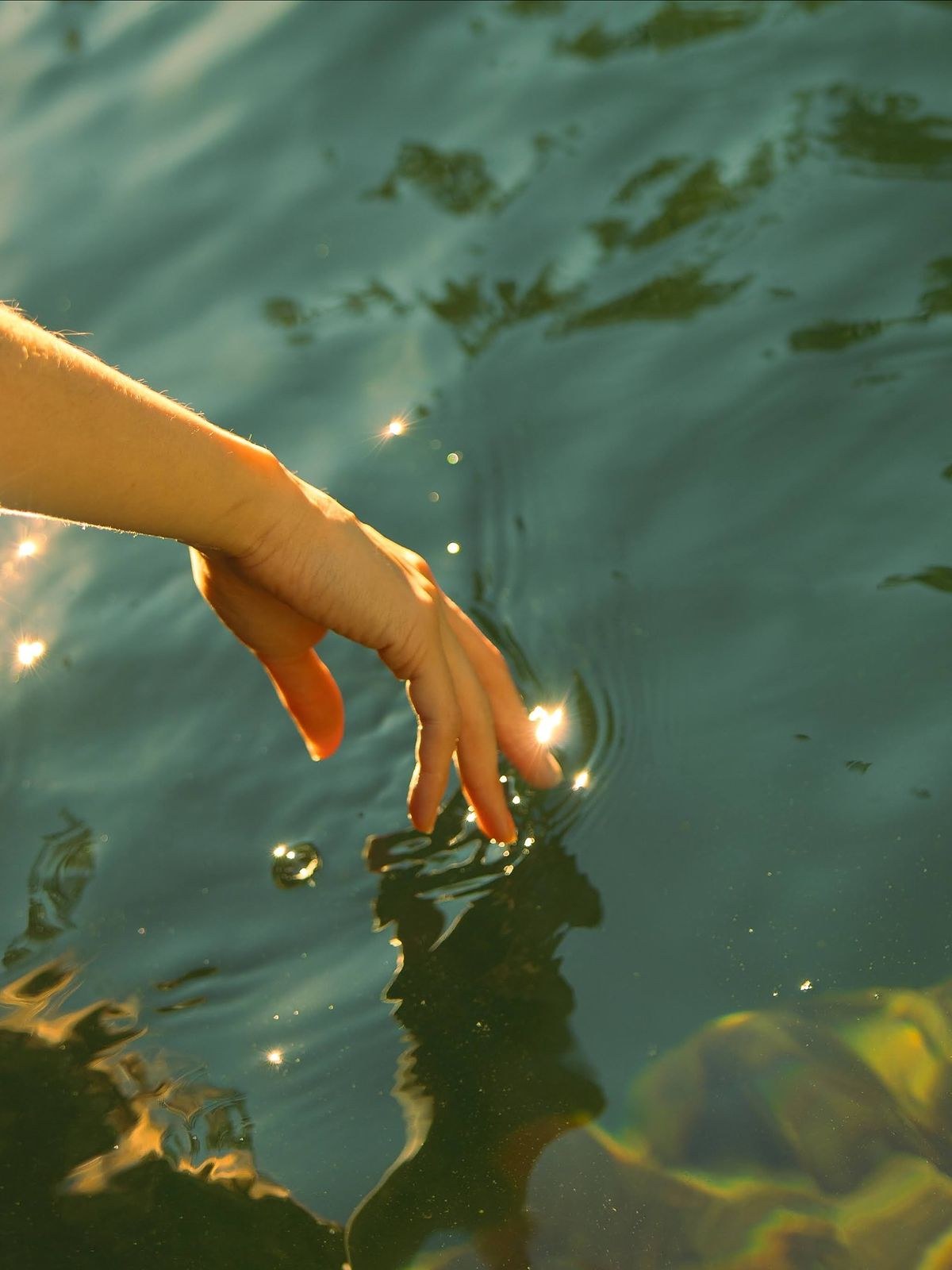 Hand touching still water with sunlight sparkles